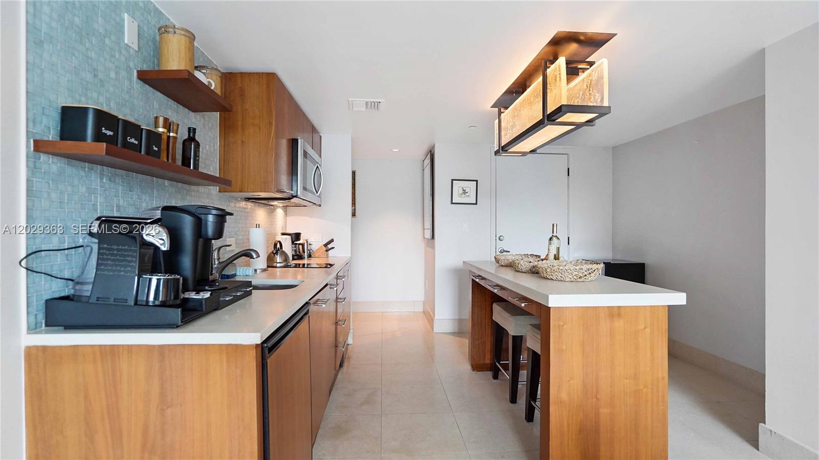A kitchen features wood cabinets, a light-colored countertop, and a breakfast bar with stools — 6801 Collins Ave # 315, Miami Beach FL 33141, MIAMI BEACH, FL