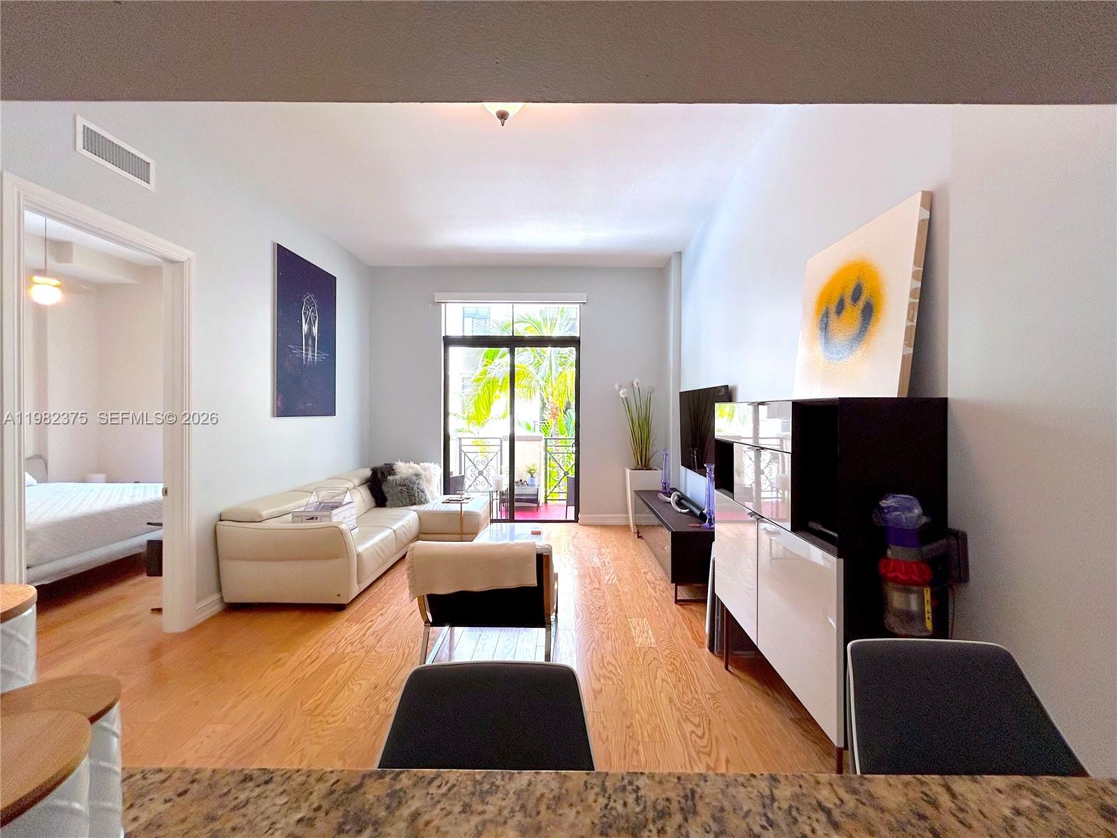 A living room features light wood flooring, a white sectional sofa, and a balcony view — 1805 Ponce De Leon Blvd # 626, Coral Gables FL 33134, CORAL GABLES, FL