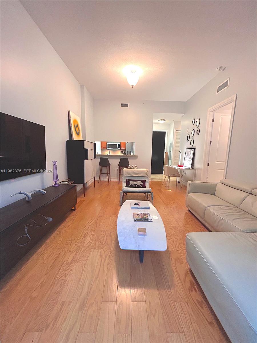 A living room with hardwood floors, a white sofa, and a kitchen pass-through window — 1805 Ponce De Leon Blvd # 626, Coral Gables FL 33134, CORAL GABLES, FL