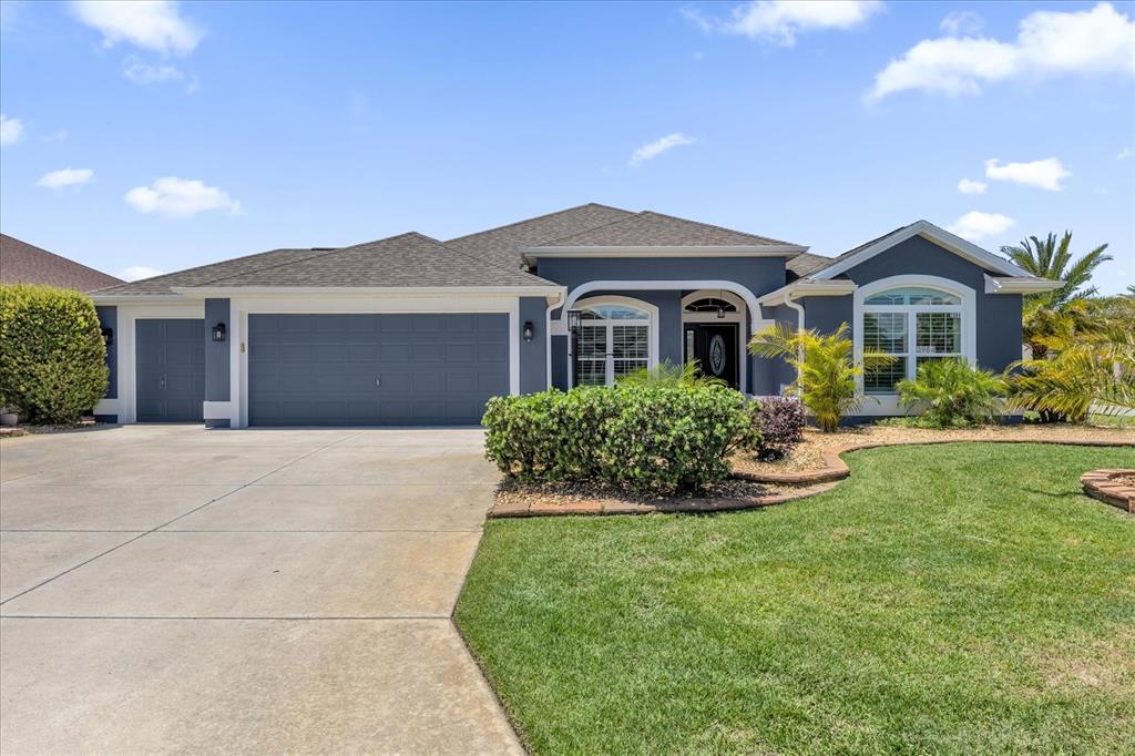 A blue single-story house with a gray roof, a three-car garage, and a landscaped lawn — 3984 MCDOWELL DRIVE, THE VILLAGES, FL