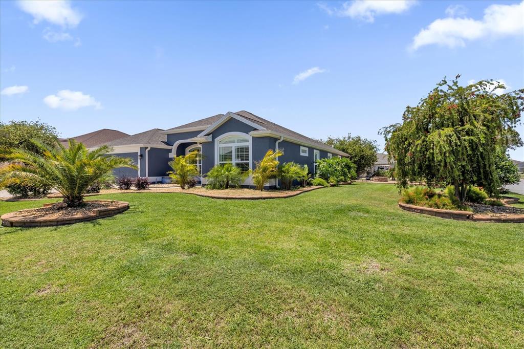 A blue single-story house with a lawn and landscaping under a blue sky — 3984 MCDOWELL DRIVE, THE VILLAGES, FL