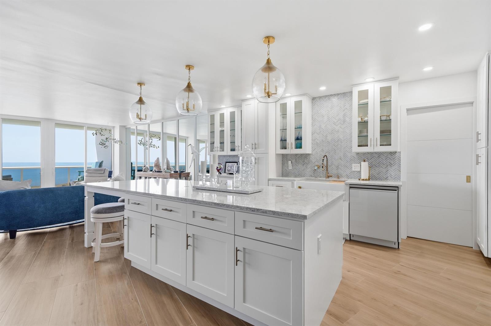 A bright kitchen features a large white island, glass-front cabinets, and a herringbone tile backsplash — 700 S Ocean Boulevard # 803, Boca Raton FL 33432, BOCA RATON, FL