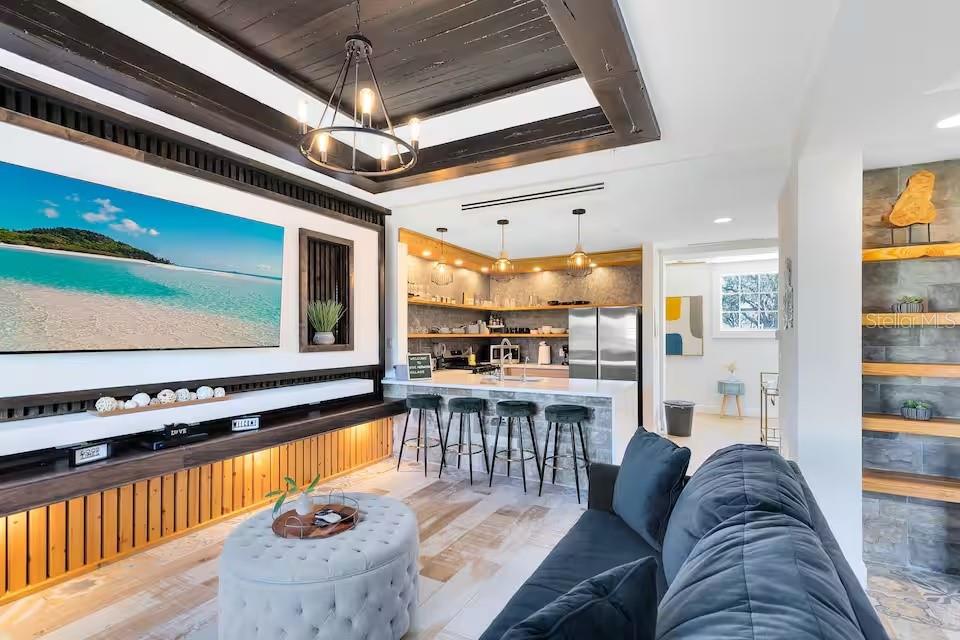 A living room with a large television, dark wood ceiling, and an open kitchen area — 1326 SEVEN EAGLES COURT UNIT 1326, KISSIMMEE, FL