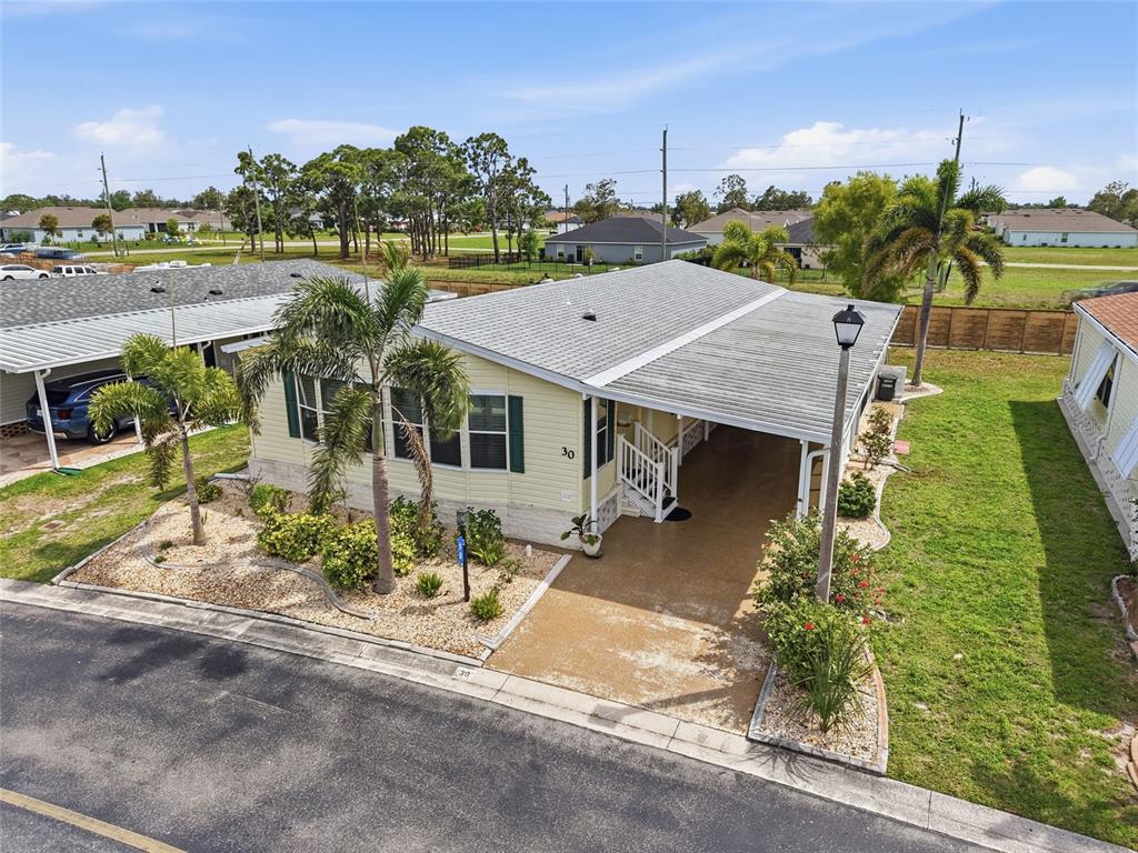 A light yellow manufactured home features a covered carport, palm trees, and a gravel garden — 15550 BURNT STORE ROAD UNIT 30, PUNTA GORDA, FL