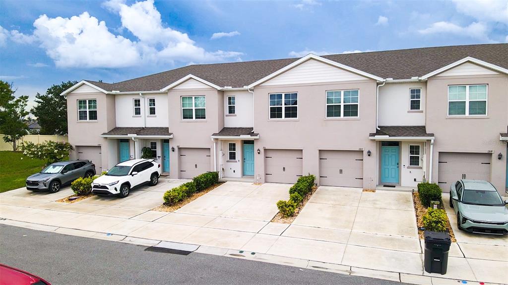 A row of multi-story townhomes with beige stucco siding, attached garages, and concrete driveways — 1311 TALLOWWOOD LANE, DAVENPORT, FL