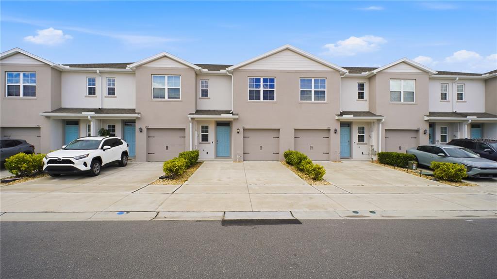 A row of multi-story townhomes with light-colored stucco facades, blue doors, and attached garages — 1311 TALLOWWOOD LANE, DAVENPORT, FL