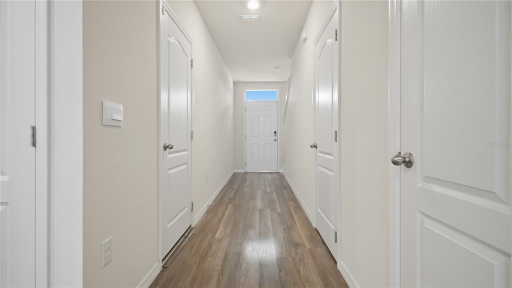 A hallway with light-colored walls, wood-look flooring, and several white interior doors — 1311 TALLOWWOOD LANE, DAVENPORT, FL