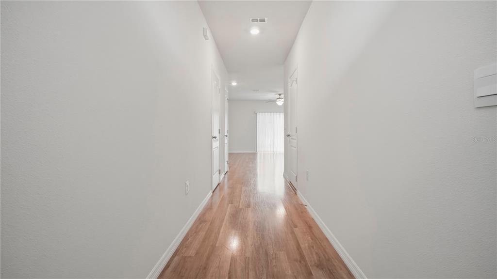A long hallway with light wood flooring leads to a room with a sliding glass door — 1311 TALLOWWOOD LANE, DAVENPORT, FL