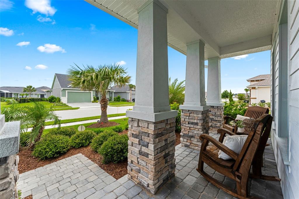 A covered front porch features stone-based columns, paver flooring, and two wooden rocking chairs — 257 MOSAIC BOULEVARD, DAYTONA BEACH, FL