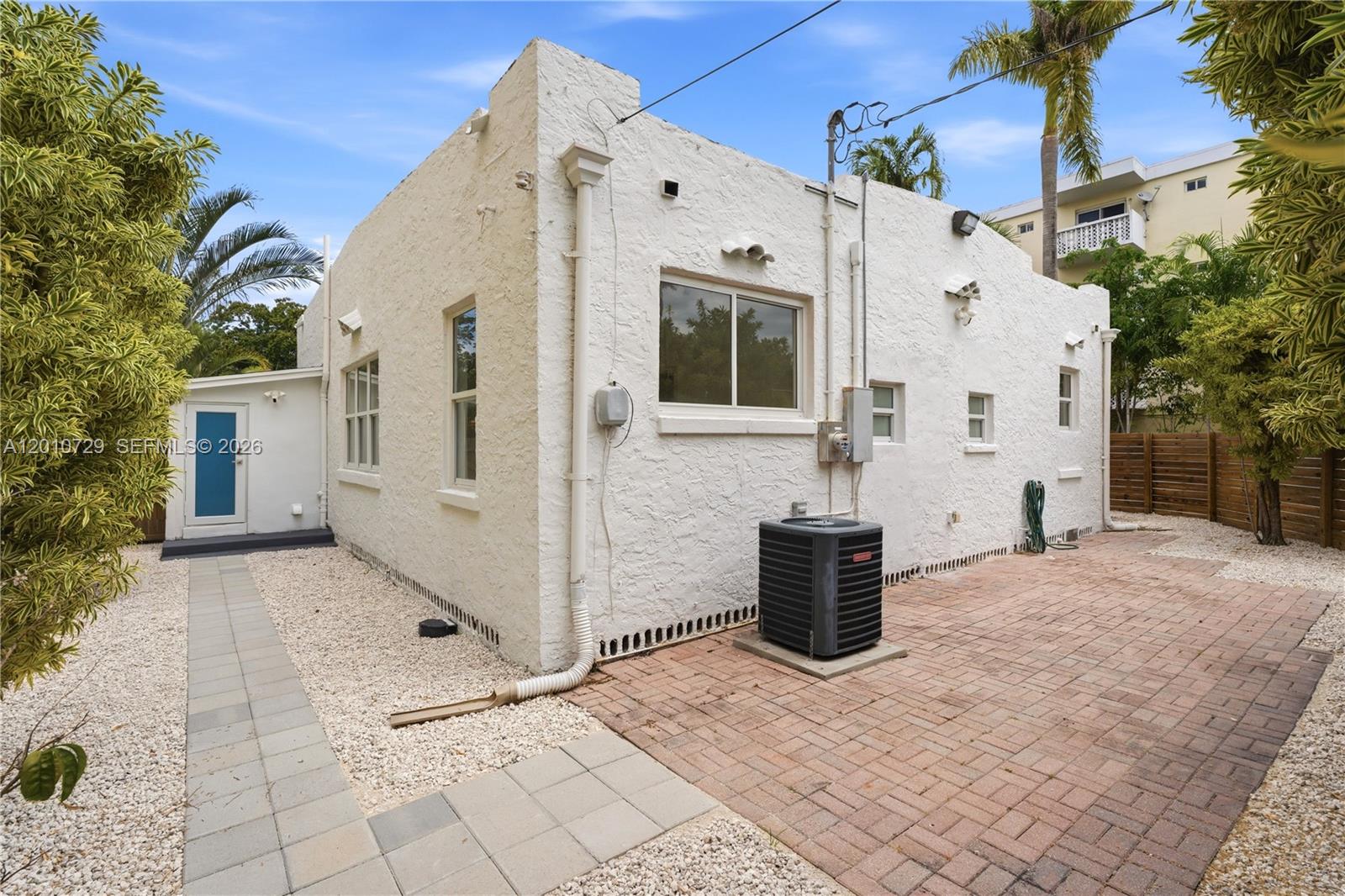 The exterior of a white stucco house features a brick patio, gravel, and an AC unit — 340 NE 125th St, North Miami FL 33161, NORTH MIAMI, FL