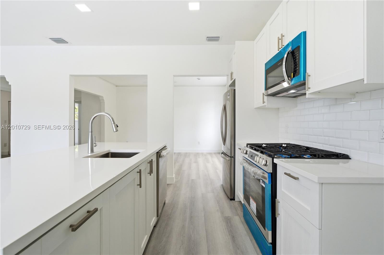 A modern kitchen features white cabinets, stainless steel appliances, and a quartz-topped island — 340 NE 125th St, North Miami FL 33161, NORTH MIAMI, FL