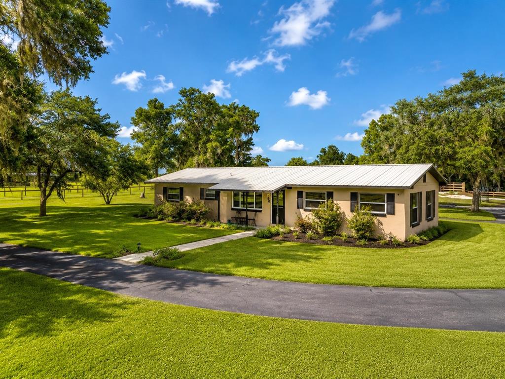 A single-story house with a metal roof sits on a grassy lot with trees — 196 NW 100TH AVENUE, OCALA, FL