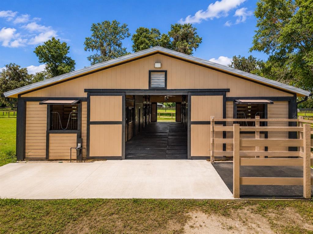 A tan horse barn with black trim and sliding doors opens to a central aisle — 196 NW 100TH AVENUE, OCALA, FL