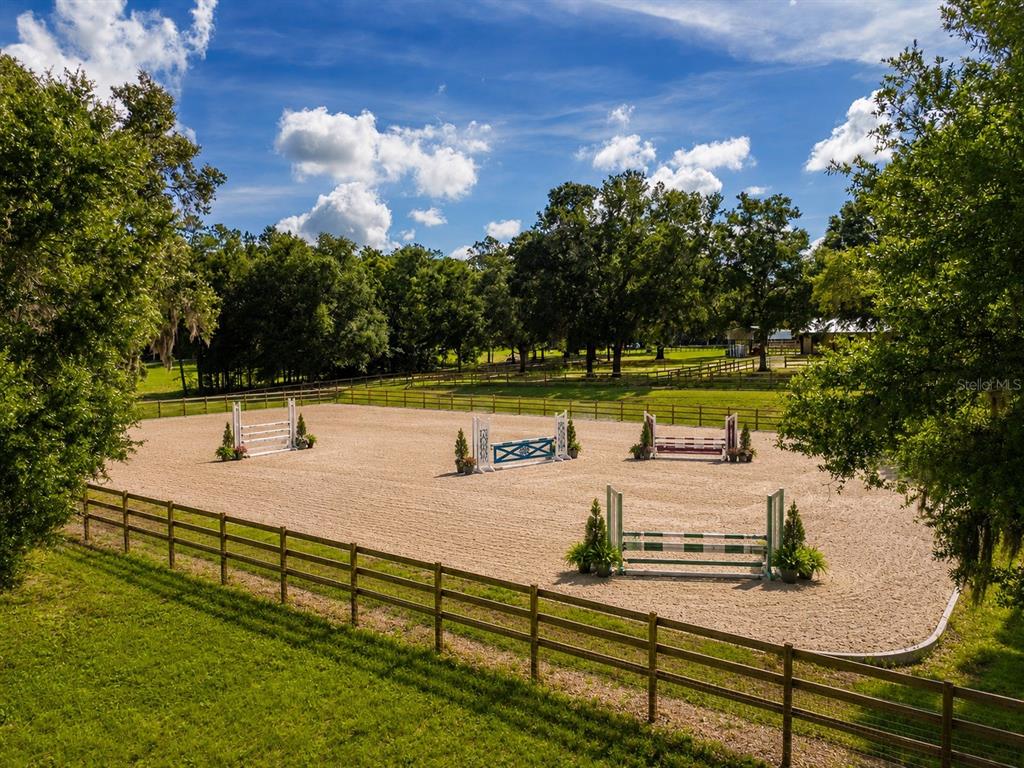 An outdoor equestrian riding arena with several jumps enclosed by a wooden fence — 196 NW 100TH AVENUE, OCALA, FL