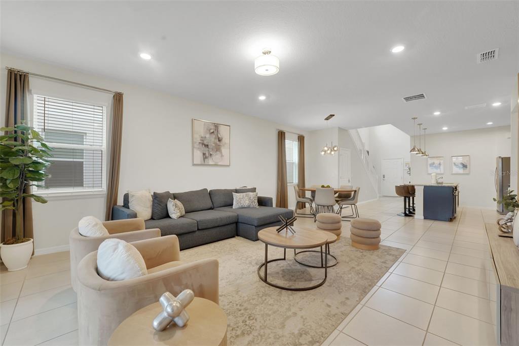 An open-concept living and dining area features a gray sectional, beige armchairs, and tile flooring — 4450 KAIPO ROAD, DAVENPORT, FL