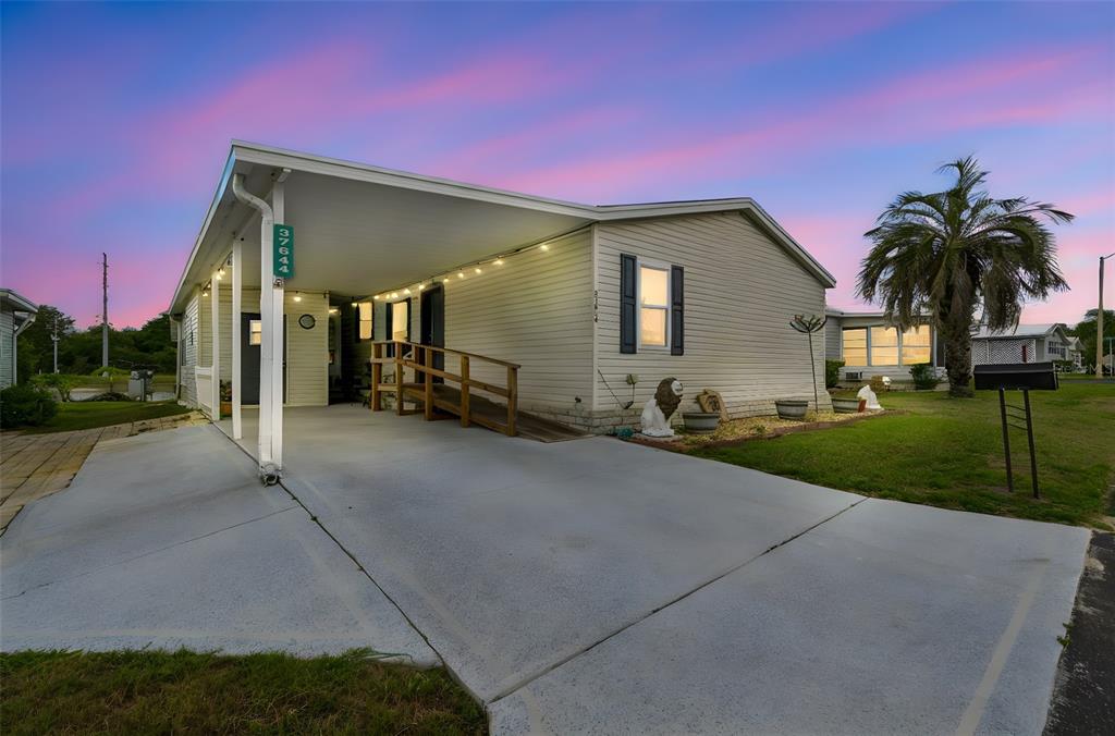A single-story mobile home with a carport, wheelchair ramp, and a palm tree at sunset — 37644 PINATA AVENUE, ZEPHYRHILLS, FL