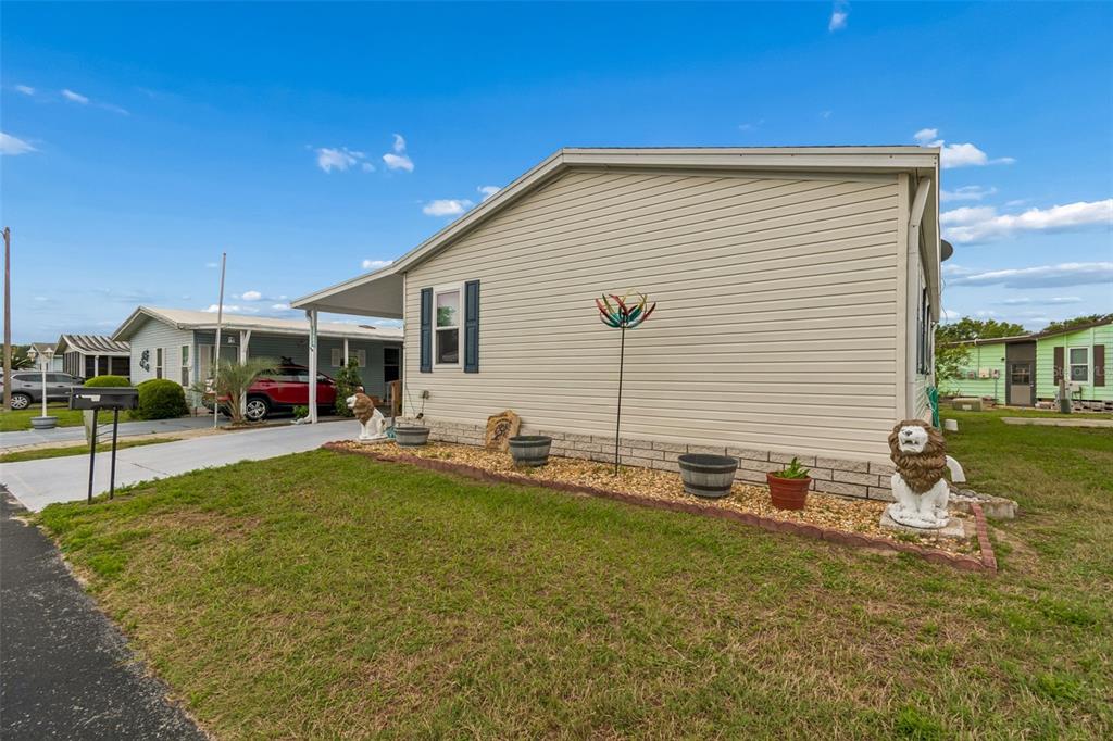 A beige mobile home with a carport, gravel landscaping, and lion statues in the yard — 37644 PINATA AVENUE, ZEPHYRHILLS, FL