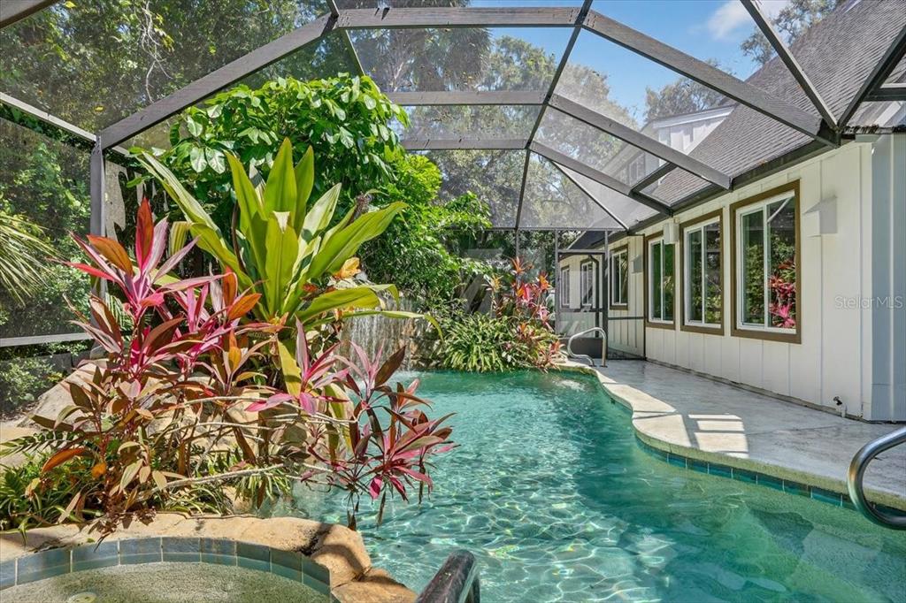 A screened-in swimming pool area features a rock waterfall, lush tropical plants, and a patio — 120 BEACH STREET, PONCE INLET, FL