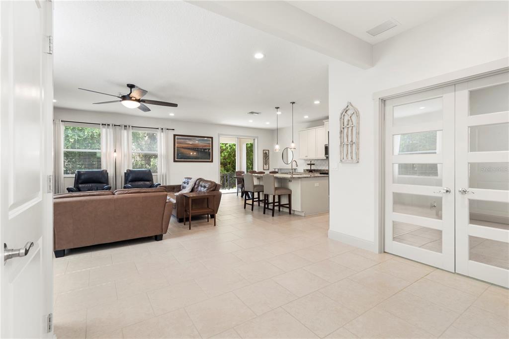 An open-concept living room and kitchen featuring tile flooring, white cabinetry, and glass-paneled doors — 6311 HORSE MILL PLACE, PALMETTO, FL