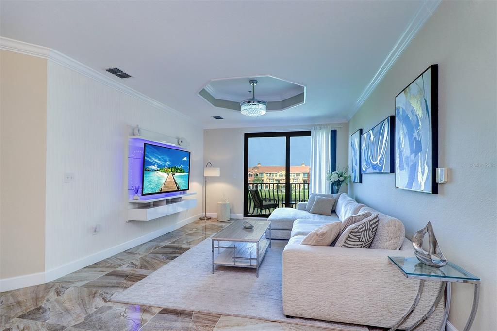 A living room features a wall-mounted television, a sectional sofa, and tile flooring — 2722 VIA TIVOLI UNIT 435B, CLEARWATER, FL