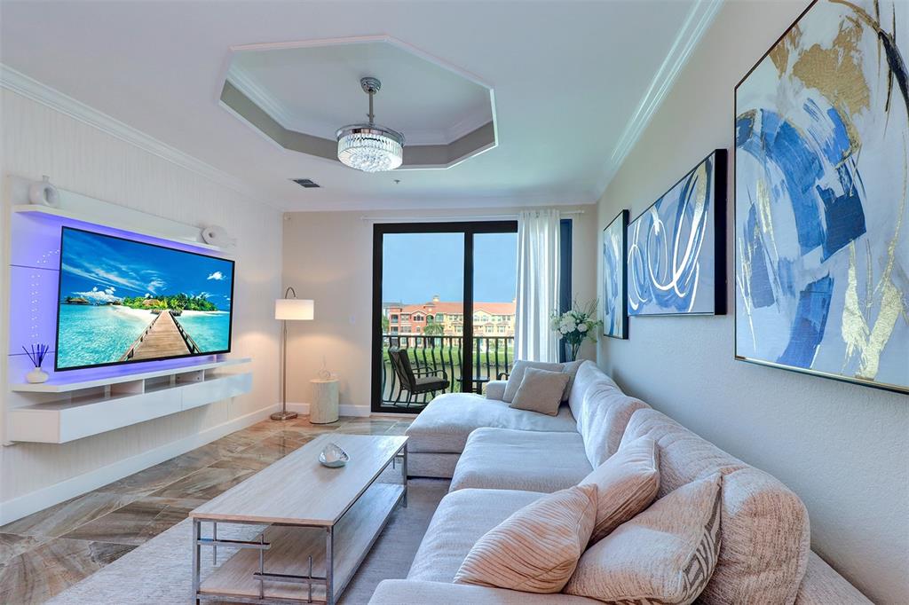 A living room features a wall-mounted television, a sectional sofa, and a balcony view — 2722 VIA TIVOLI UNIT 435B, CLEARWATER, FL