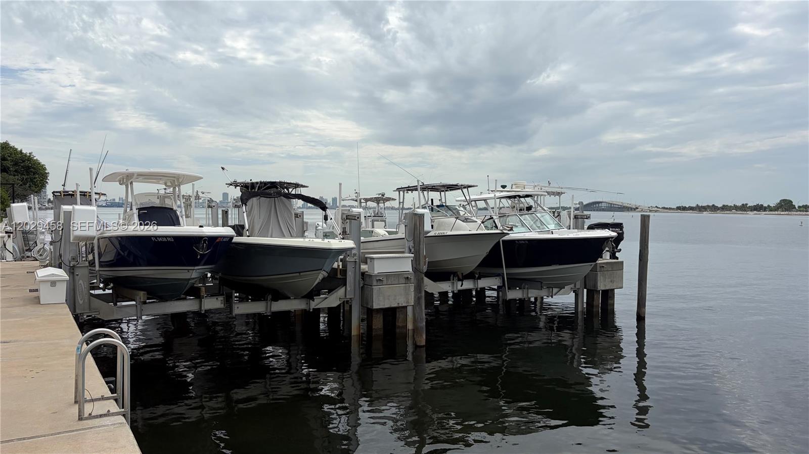 Several motorboats are docked on lifts along a concrete pier under a cloudy sky — 150 SE 25th Rd, Miami FL 33131, MIAMI, FL