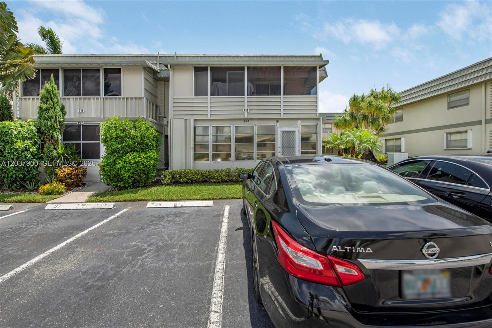 A two-story apartment building exterior features screened balconies and a parking lot with cars — 712 Monaco O # 712, Delray Beach FL 33446, DELRAY BEACH, FL