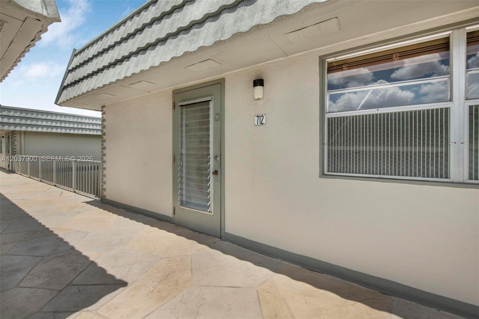A beige exterior wall features a door numbered 712, a window, and a tiled walkway — 712 Monaco O # 712, Delray Beach FL 33446, DELRAY BEACH, FL