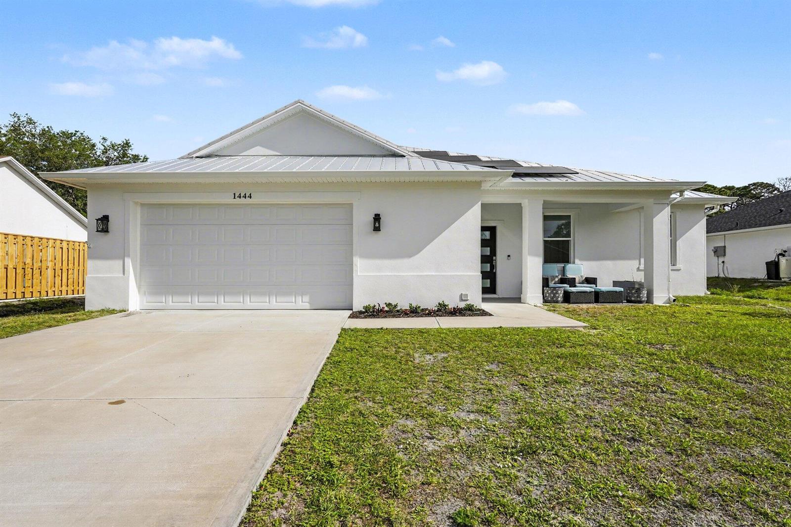 A white single-story house with a metal roof, two-car garage, and a covered front porch — 1444 Seeley Circle NW, Palm Bay FL 32907, PALM BAY, FL