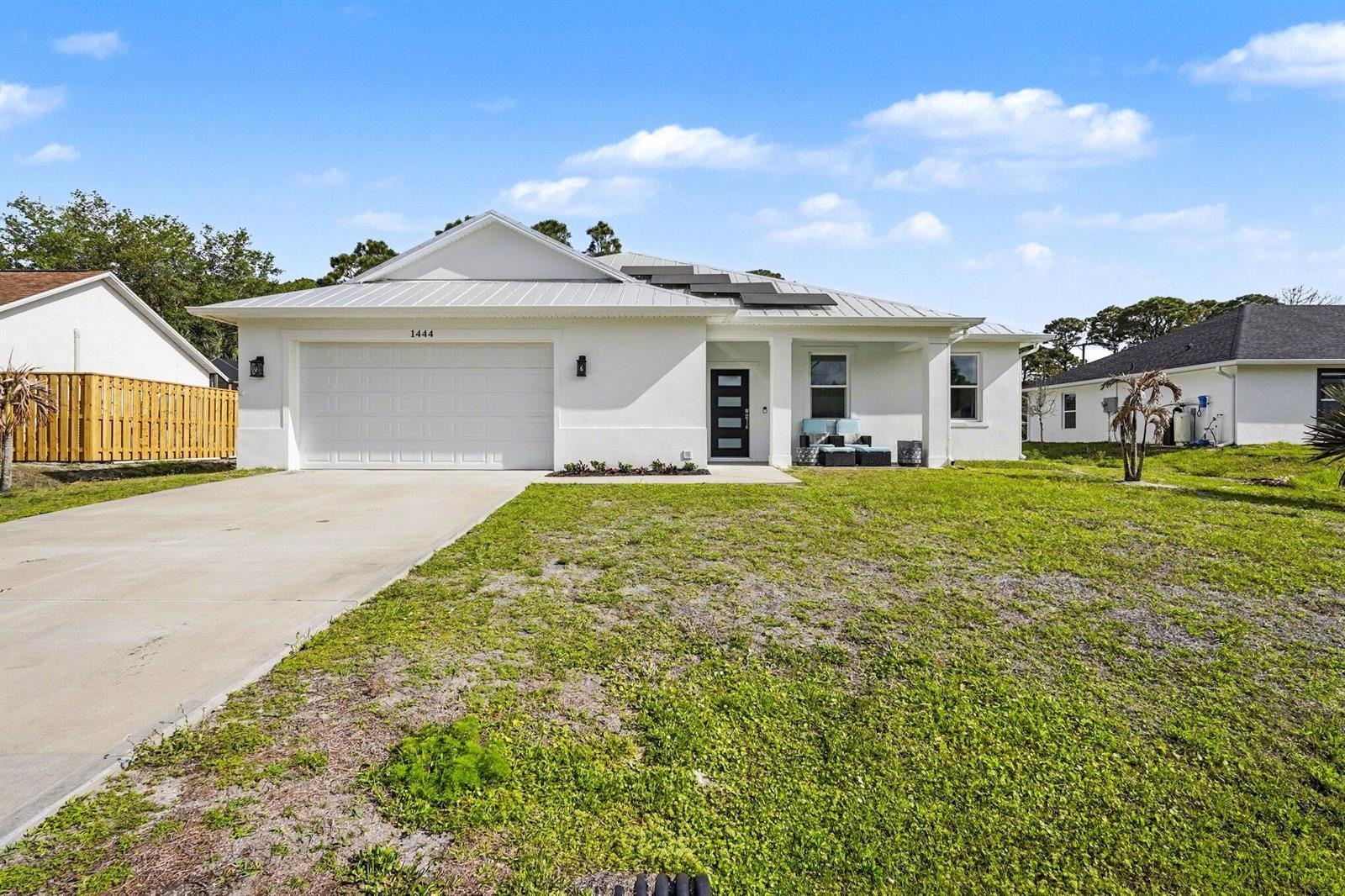 A white single-story house features a metal roof, solar panels, and a concrete driveway — 1444 Seeley Circle NW, Palm Bay FL 32907, PALM BAY, FL
