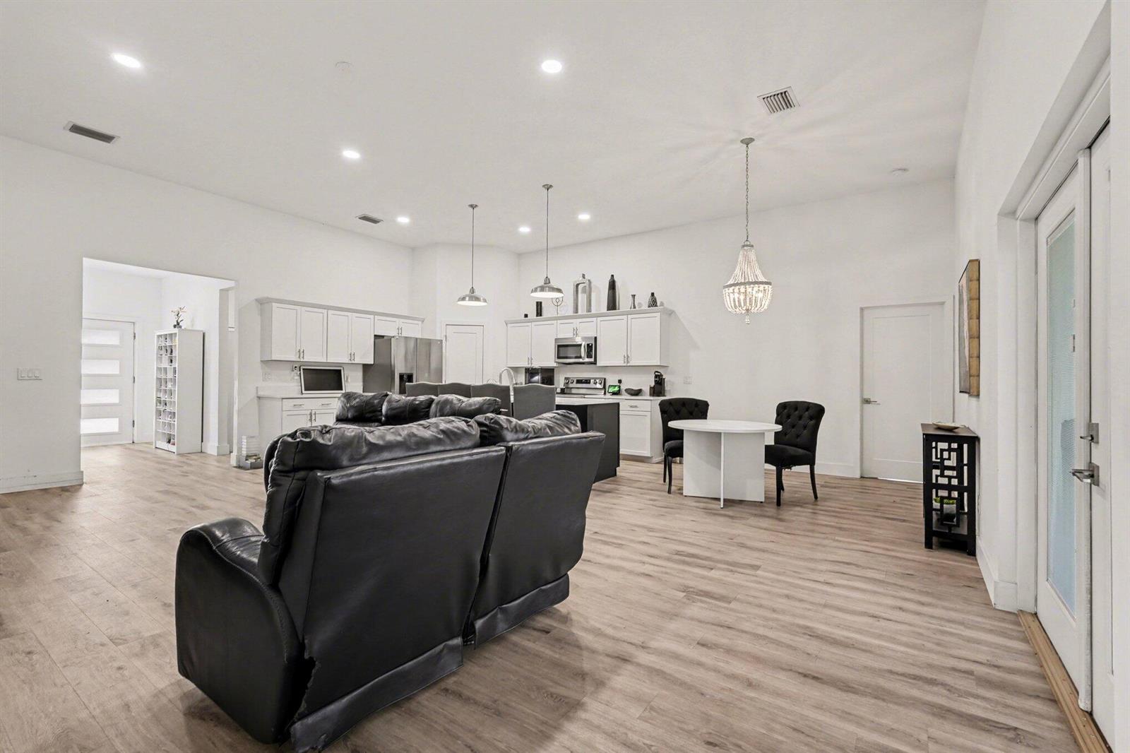 An open-concept kitchen and living area with white cabinetry, a black sofa, and wood flooring — 1444 Seeley Circle NW, Palm Bay FL 32907, PALM BAY, FL