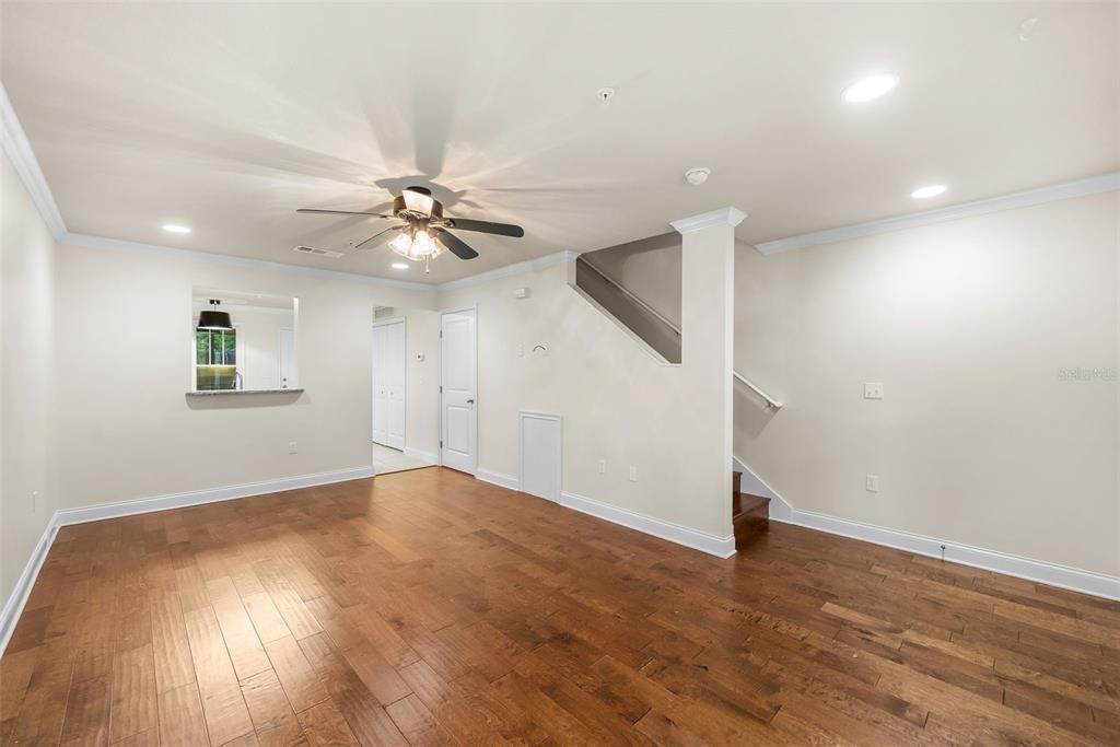 An empty living room features hardwood floors, a ceiling fan, and stairs leading upward — 4605 SW 48TH DRIVE UNIT 155, GAINESVILLE, FL