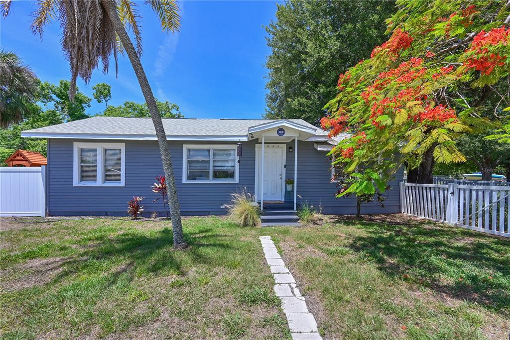 A single-story gray house with a white front door, a walkway, and a flowering tree — 1423 12TH AVENUE W, PALMETTO, FL