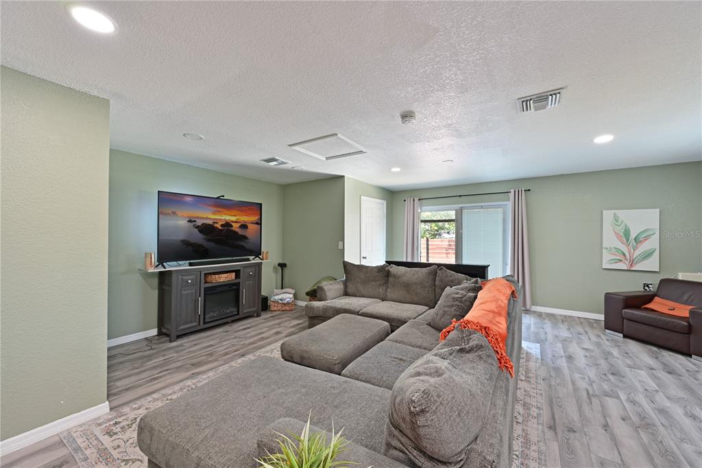 A living room features a grey sectional sofa, a television console, and light wood flooring — 1423 12TH AVENUE W, PALMETTO, FL