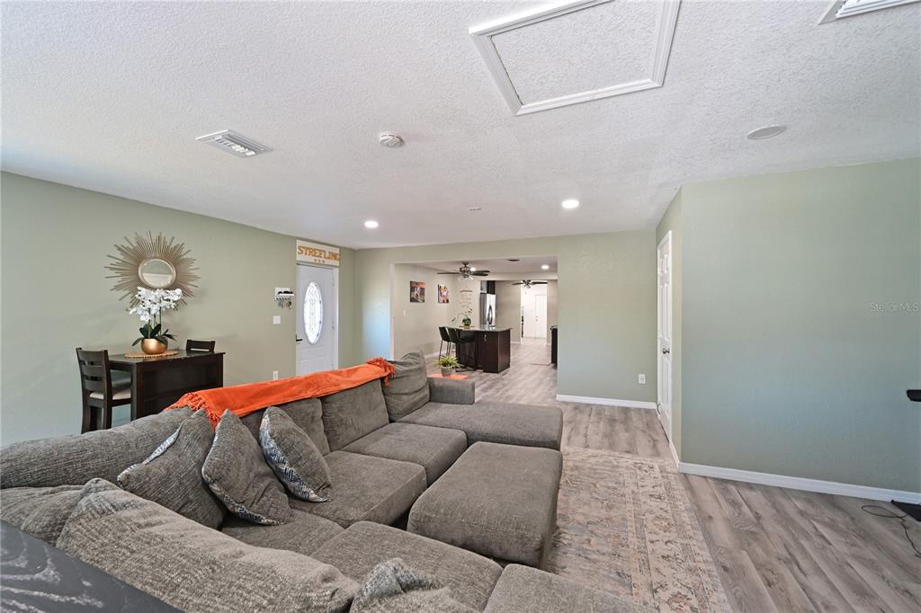 A living room with a gray sectional sofa, light wood-look flooring, and sage green walls — 1423 12TH AVENUE W, PALMETTO, FL