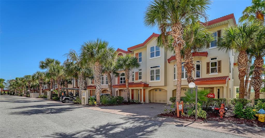 A multi-story townhouse with a paved driveway, two garage doors, and several palm trees — 221 17TH STREET N, BRADENTON BEACH, FL
