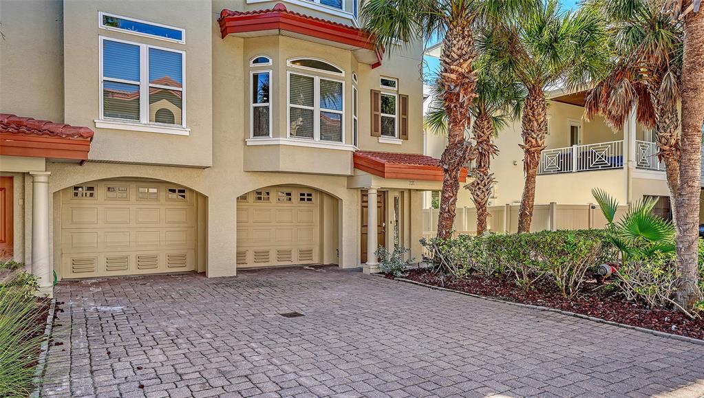 A beige multi-story townhouse features two garage doors and a brick-paved driveway — 221 17TH STREET N, BRADENTON BEACH, FL
