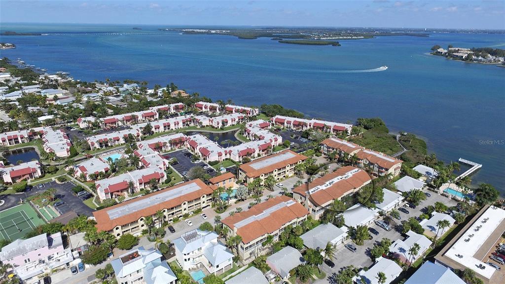 An aerial view shows a waterfront condominium complex with multiple buildings, parking lots, and pools — 221 17TH STREET N, BRADENTON BEACH, FL