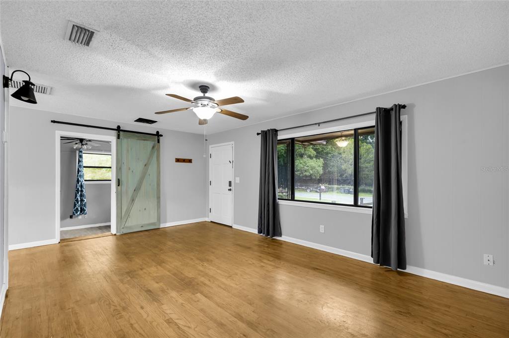 A living room features light wood flooring, gray walls, a ceiling fan, and a barn door — 1474 NE 59TH STREET, OCALA, FL