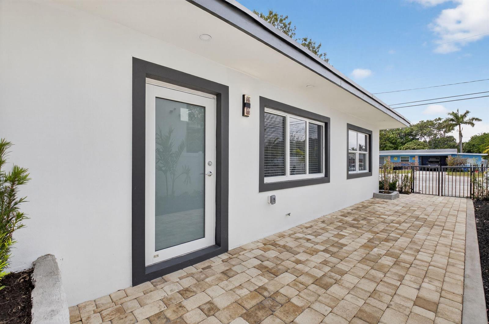A white exterior wall with a glass door, two windows, and a paved patio area — 341 SE 3rd Avenue, Delray Beach FL 33483, DELRAY BEACH, FL