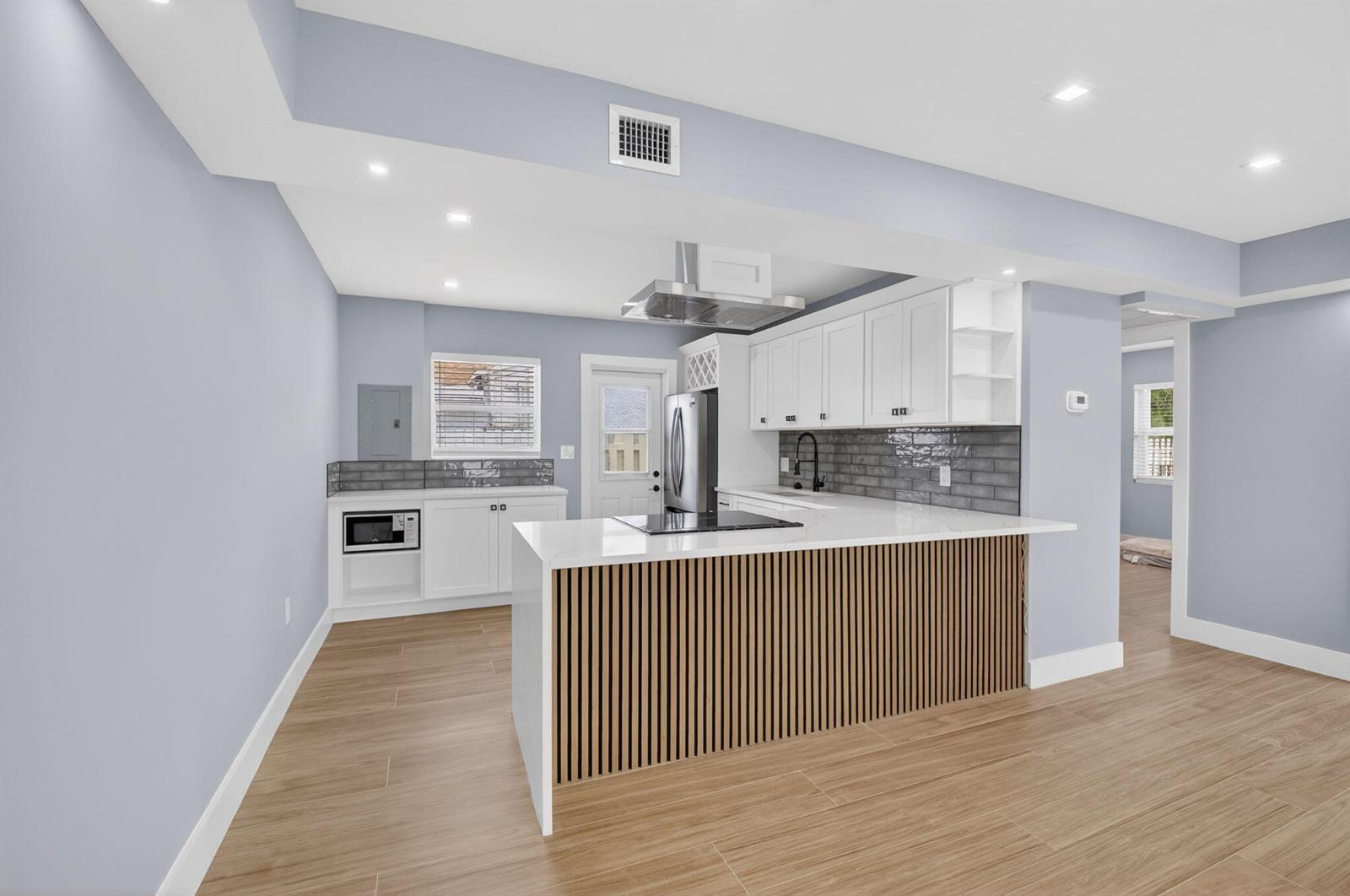 A modern kitchen features white cabinets, a slatted wood island, and gray tile backsplashes — 341 SE 3rd Avenue, Delray Beach FL 33483, DELRAY BEACH, FL