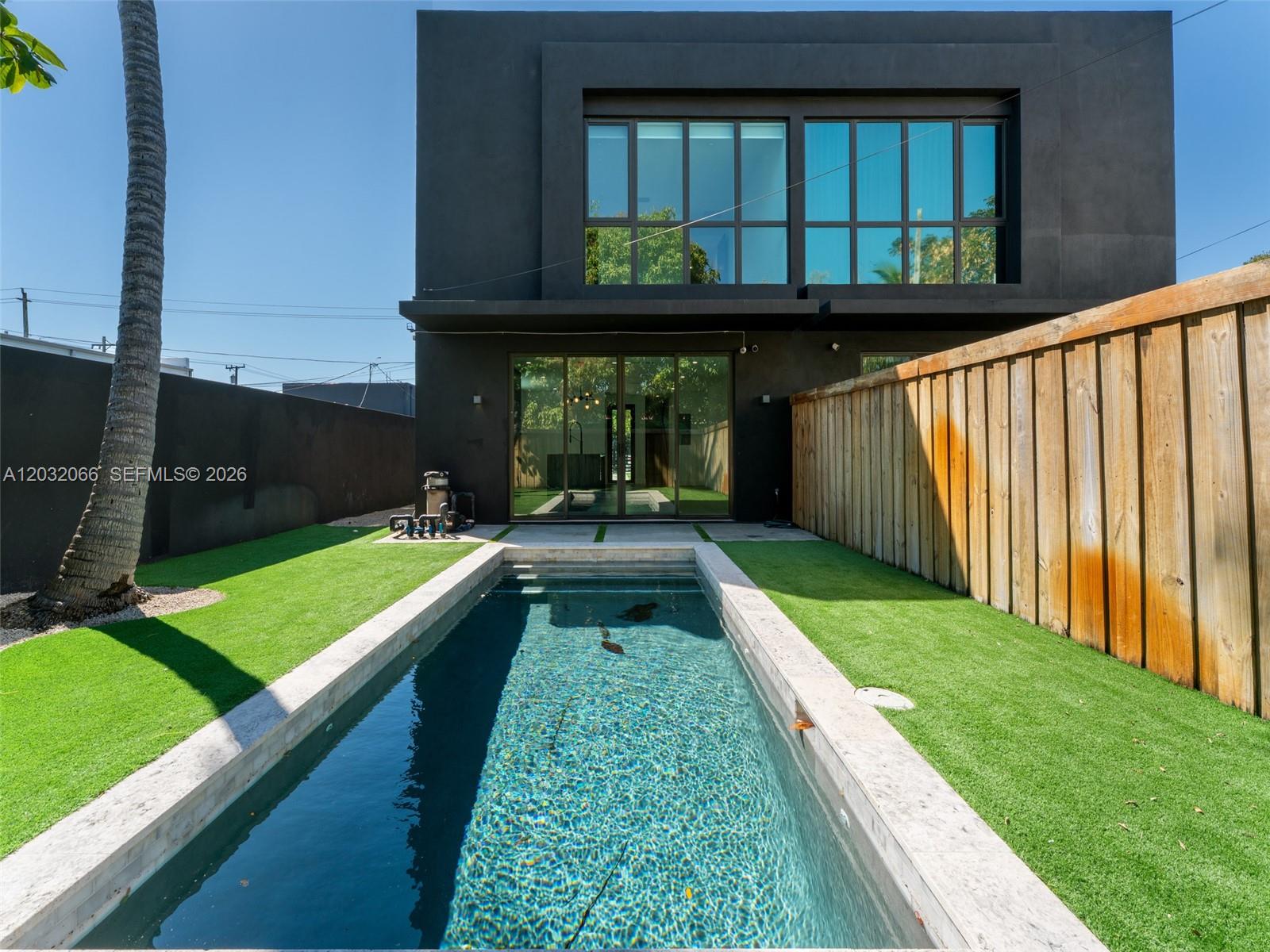 A modern black house features a rectangular swimming pool in a fenced backyard — 227 NW 39th St, Miami FL 33127, MIAMI, FL