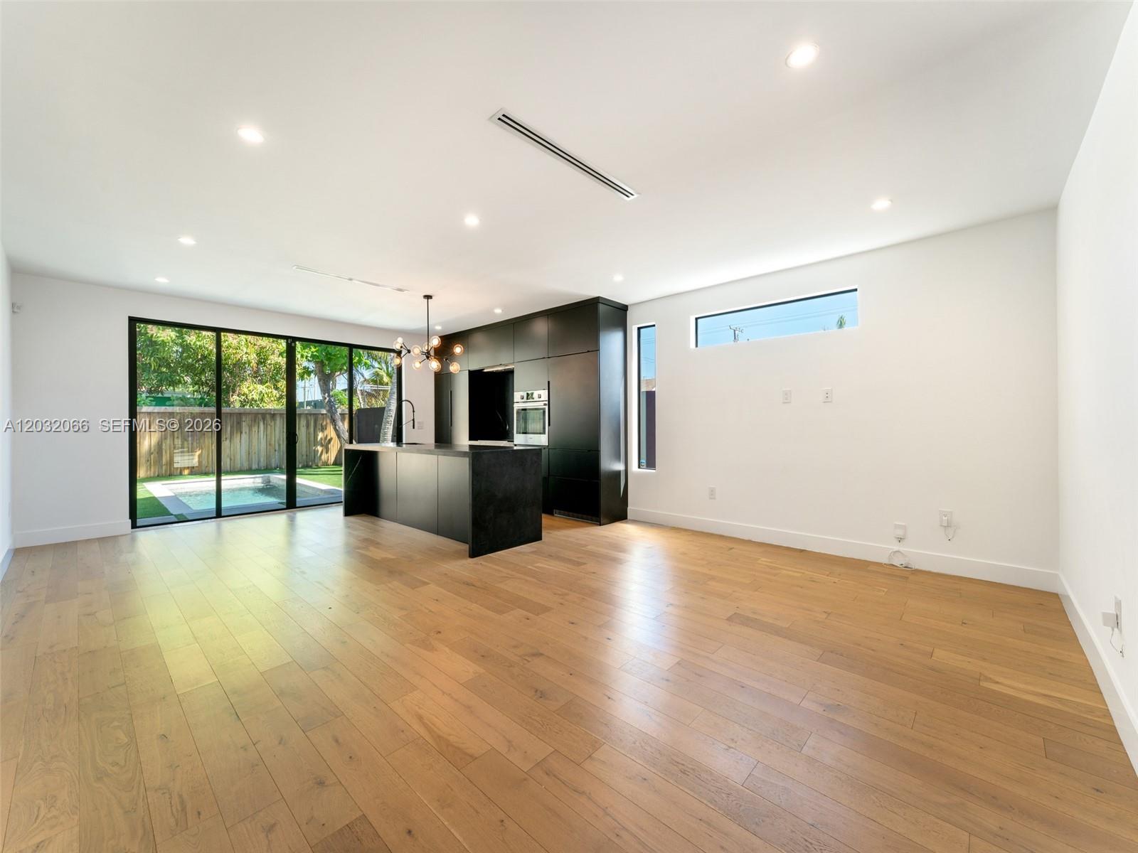 A modern kitchen with black cabinetry and an island overlooks a backyard swimming pool — 227 NW 39th St, Miami FL 33127, MIAMI, FL