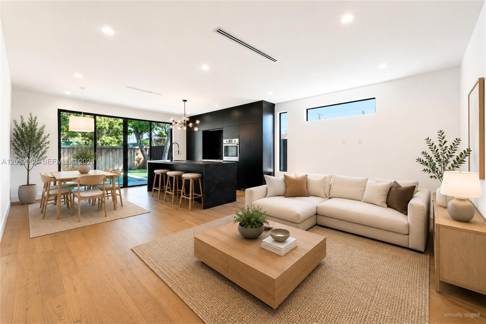 This open-concept living and dining area features a modern black kitchen and light wood floors — 227 NW 39th St, Miami FL 33127, MIAMI, FL