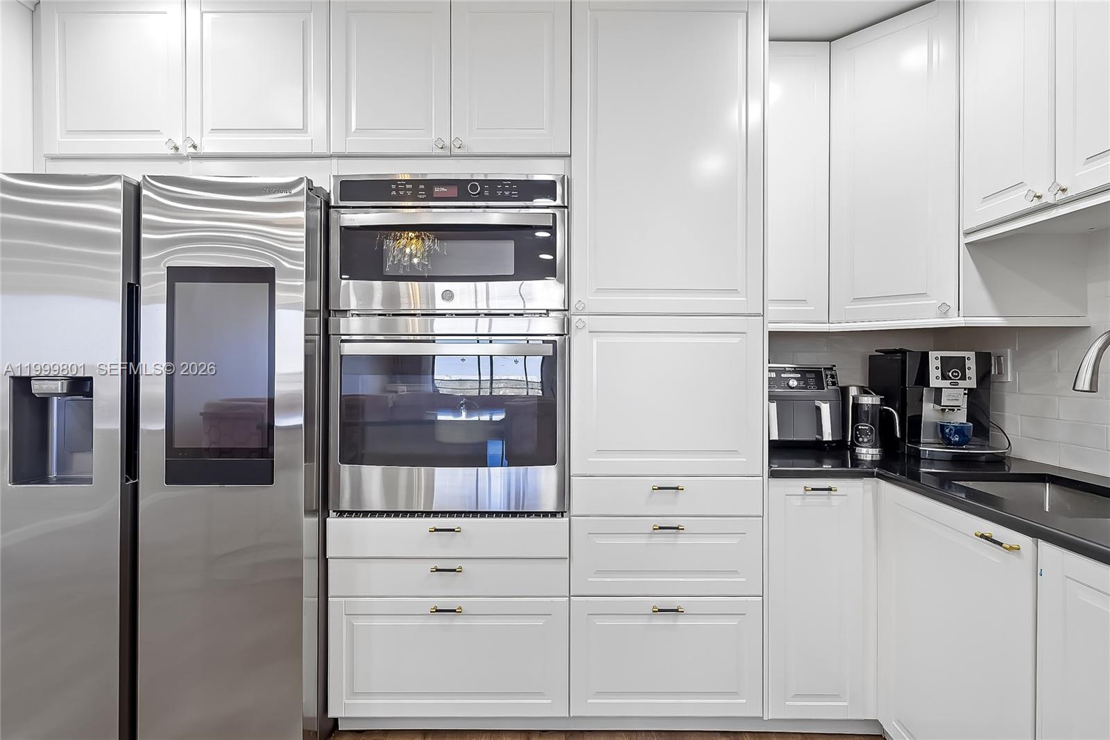 A kitchen features white cabinetry, stainless steel appliances, and black countertops — 600 Three Islands Blvd # 604, Hallandale Beach FL 33009, HALLANDALE BEACH, FL