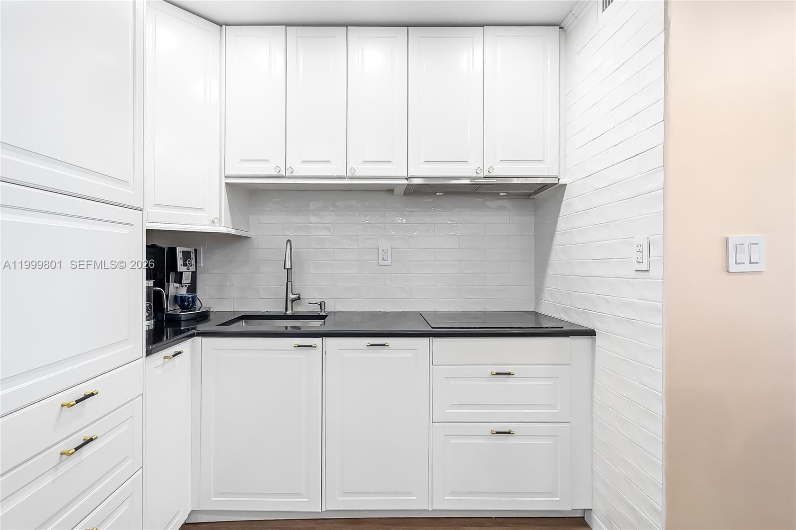 A kitchen features white cabinets, a black countertop, and a white subway tile backsplash — 600 Three Islands Blvd # 604, Hallandale Beach FL 33009, HALLANDALE BEACH, FL