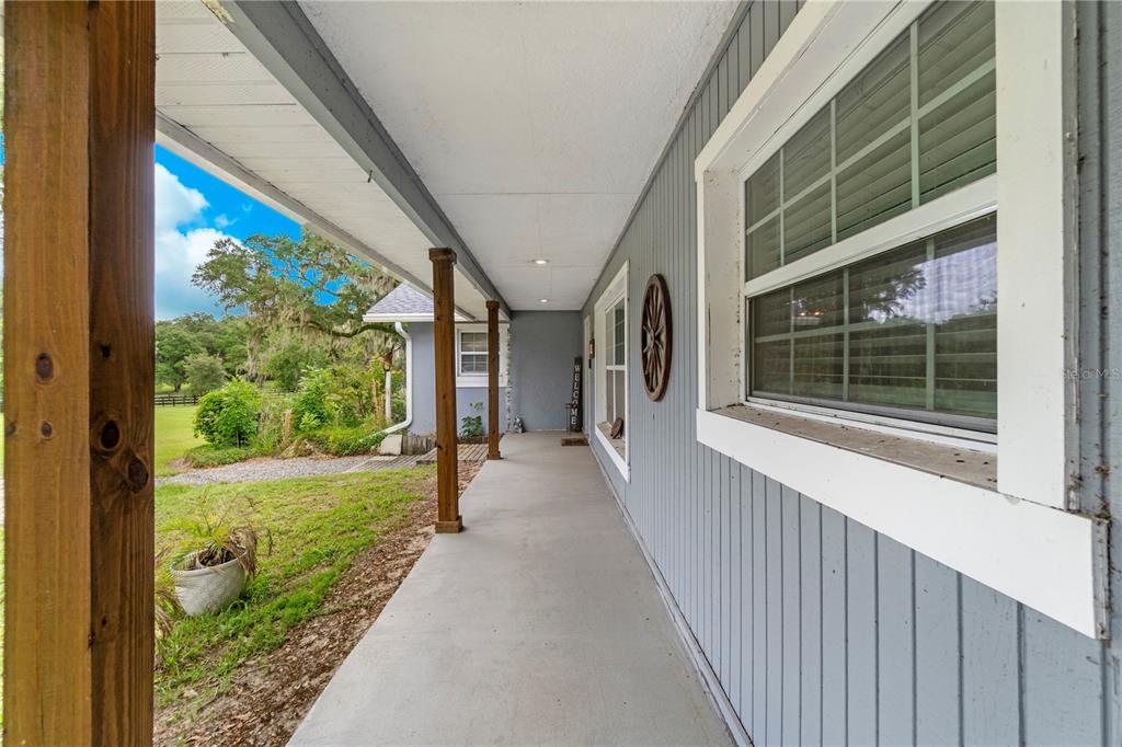 A long, covered porch with gray vertical siding, wooden support posts, and a concrete floor — 24 LAKE WOOD CIRCLE, OCALA, FL