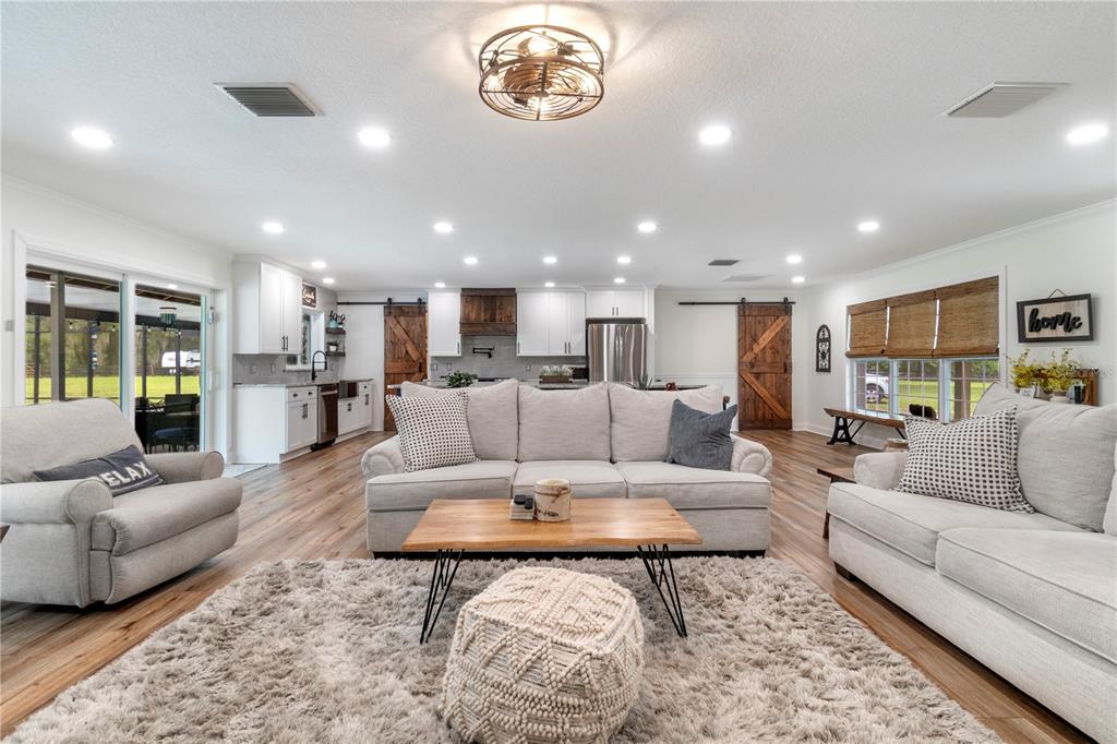 A living room with light wood floors, a shaggy rug, and a kitchen with barn doors — 24 LAKE WOOD CIRCLE, OCALA, FL