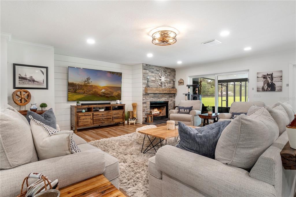 A living room features a stone fireplace, shiplap wall with a television, and neutral furniture — 24 LAKE WOOD CIRCLE, OCALA, FL