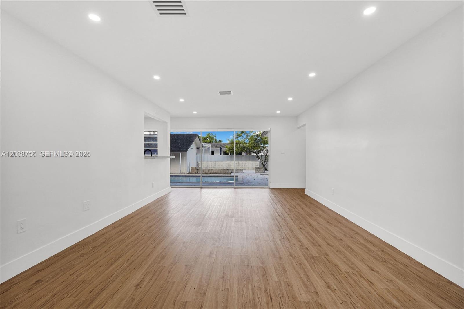 A bright, empty room features wood-look flooring, recessed lighting, and a sliding door to a pool — 8201 SW 42nd St, Miami FL 33155, MIAMI, FL
